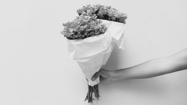 A hand holding a bouquet of flowers wrapped in paper.